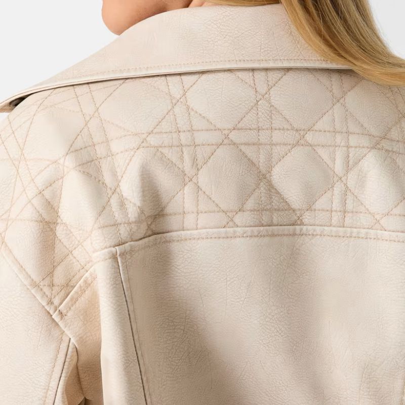 Detailed view showing the diamond-quilted stitching detail and collar texture of a cream-colored faux leather moto jacket
